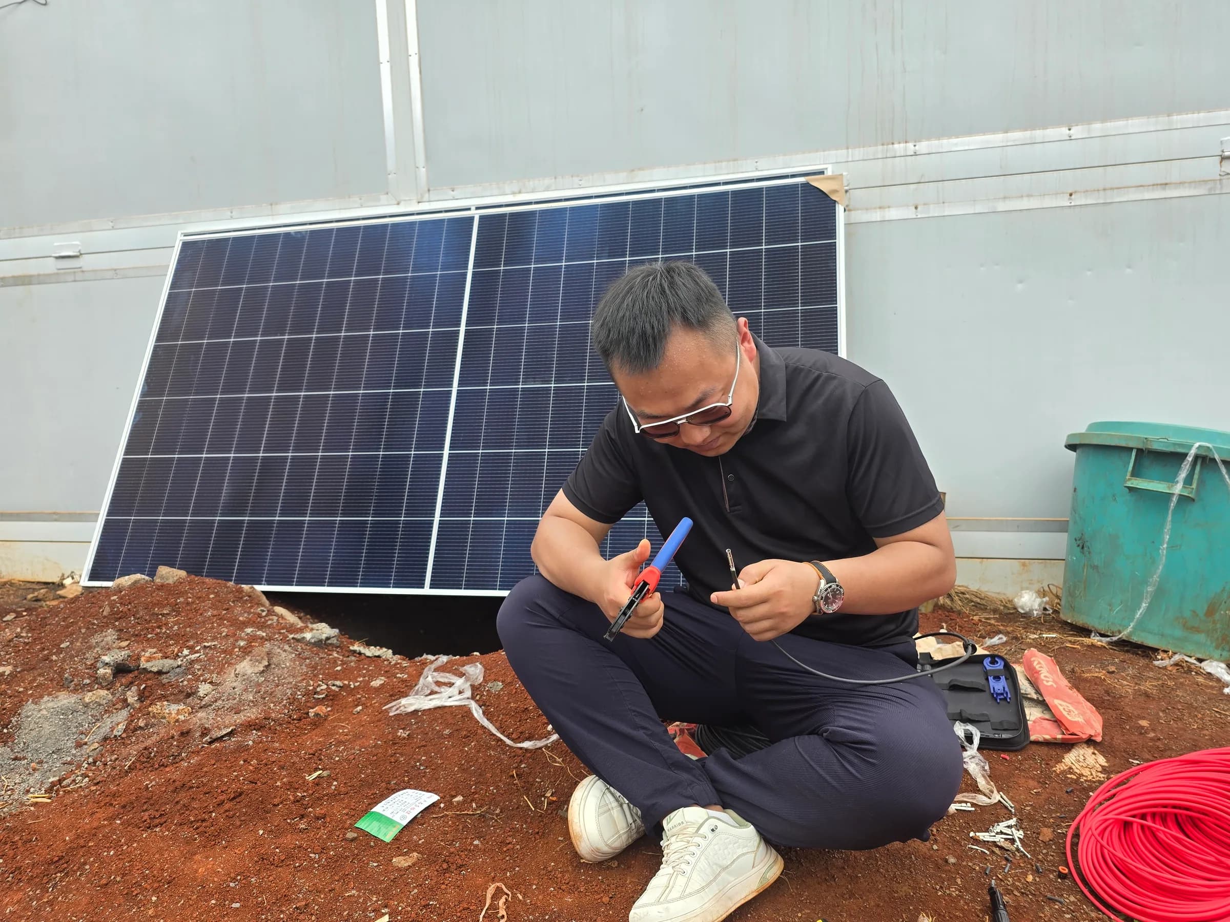Solar technician crimping a connector onto red photovoltaic cable.